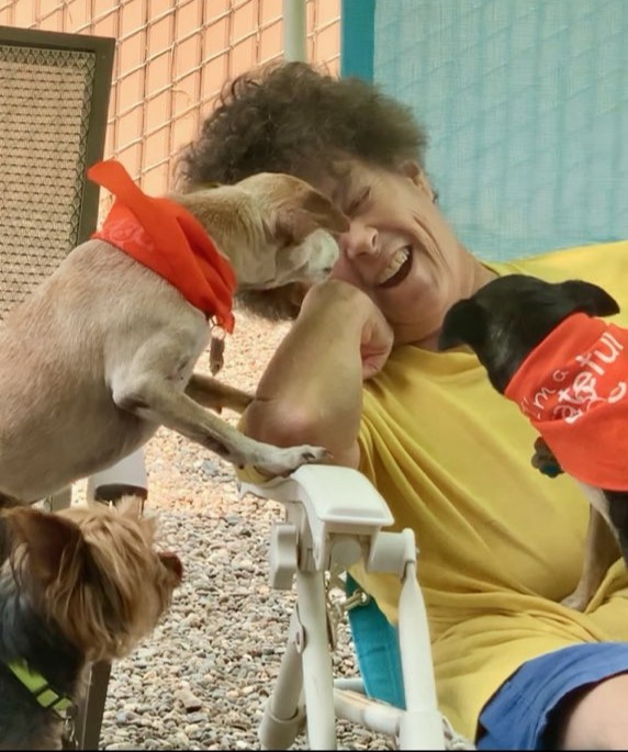 Debra the co-owner of Little Paws Doggie Rescue with three of her rescue dogs around her looking happy, with one licking her.